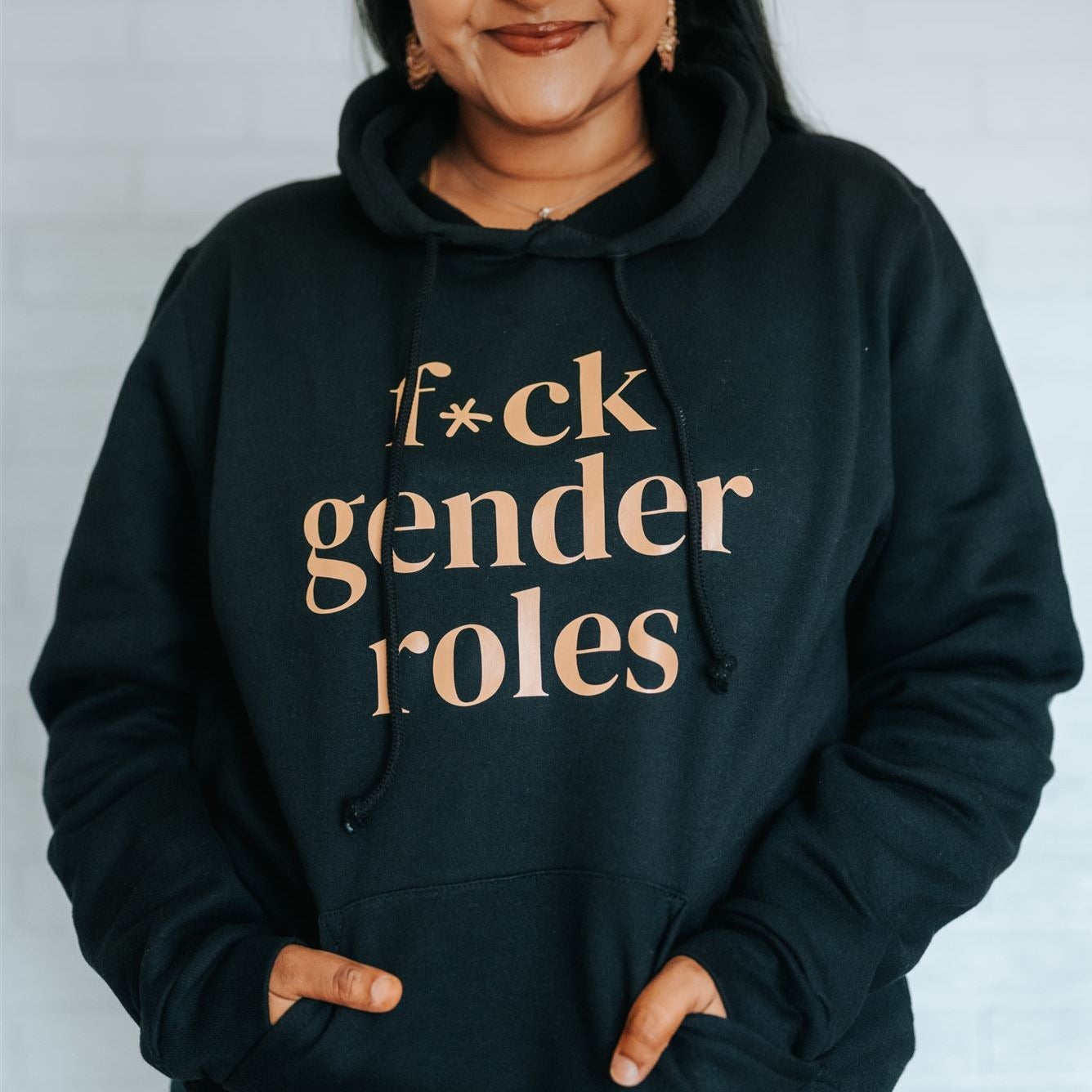 Jenny Jay is pictured wearing a black hooded sweatshirt. Sweatshirt reads 'F*ck Gender Roles' in black text.